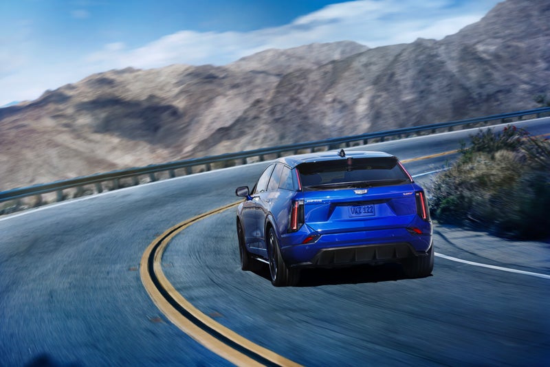 Rear View of a Blue 2026 OPTIQ-V Driving on a Curve of a Mountain Row | Hansen Motor Co Cadillac in Brigham City UT